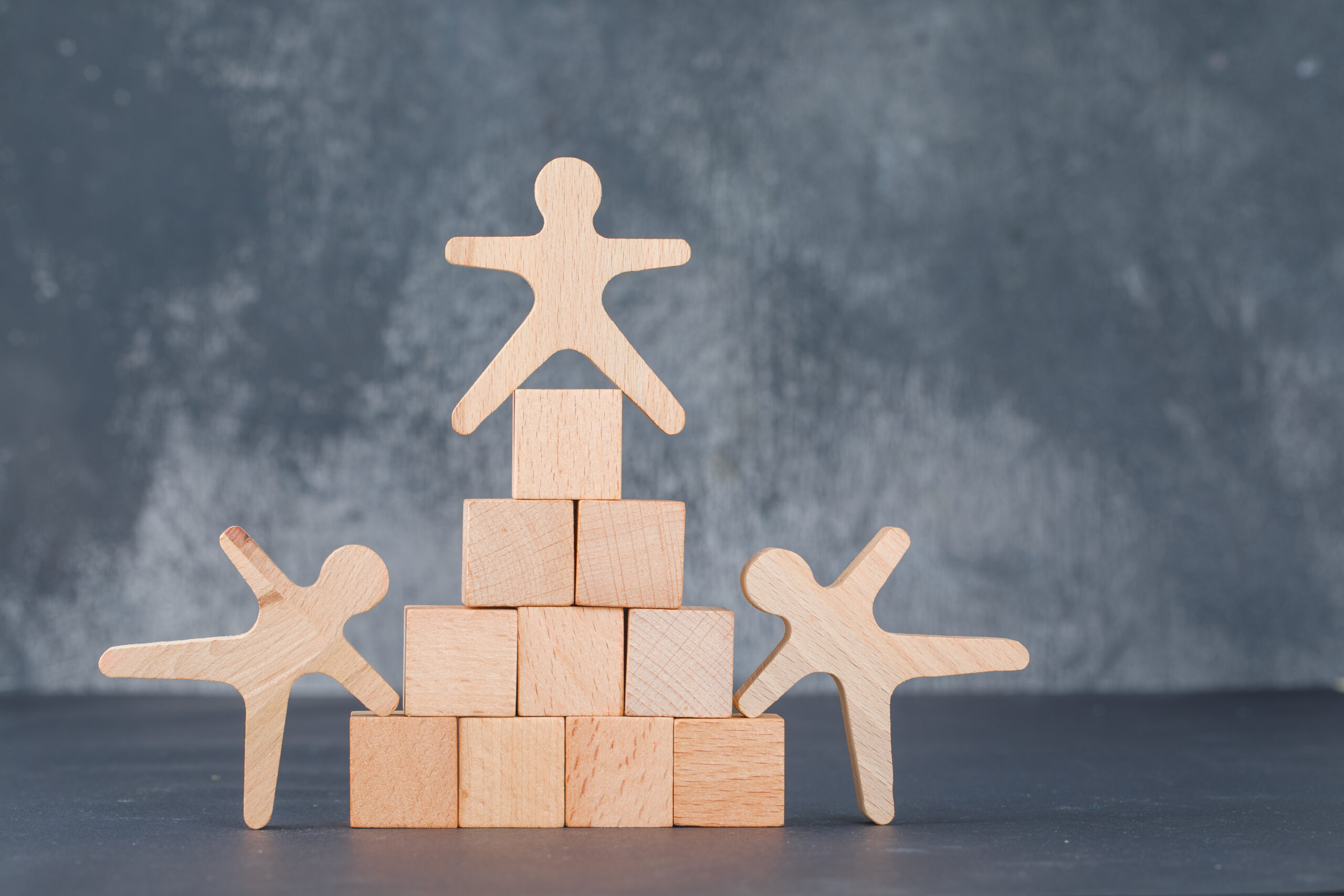 Team and business concept with wooden blocks like pyramid with wooden human figures on dark color background side view. space for text. horizontal image